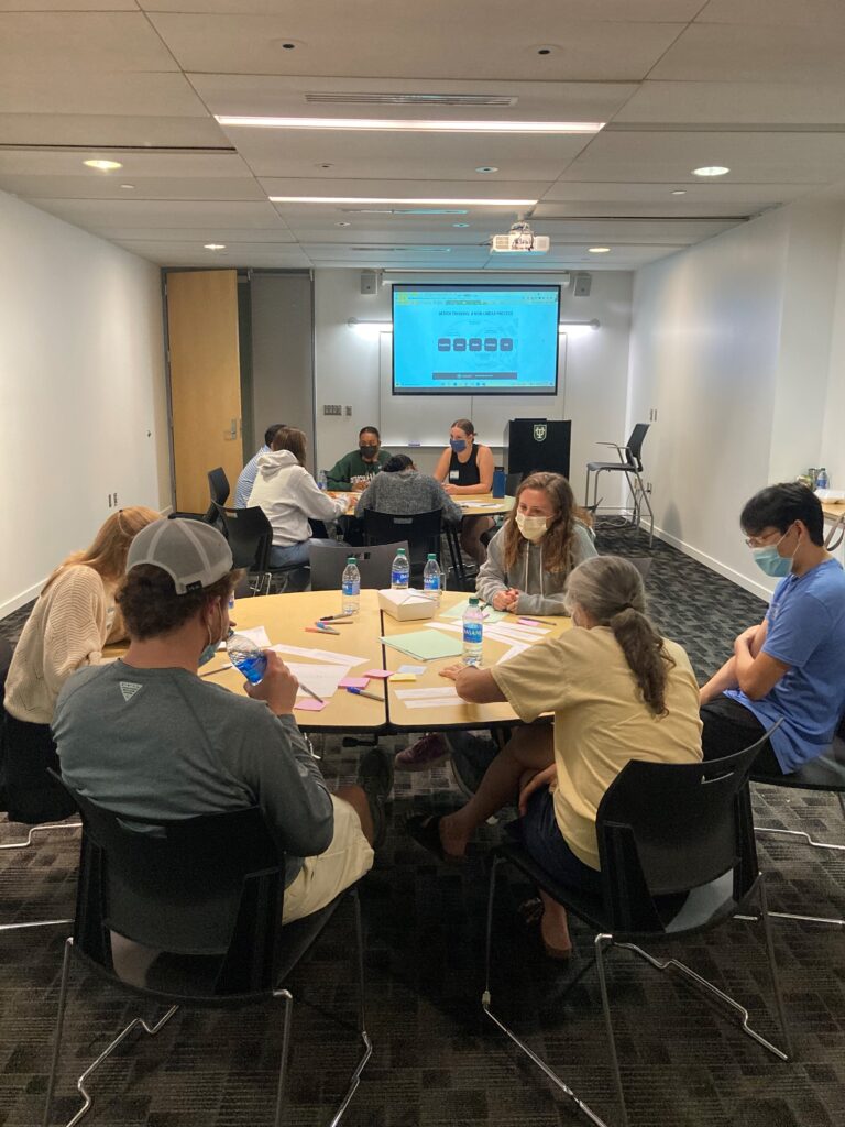 Two groups of people sitting around round tables in a room with a projector screen
